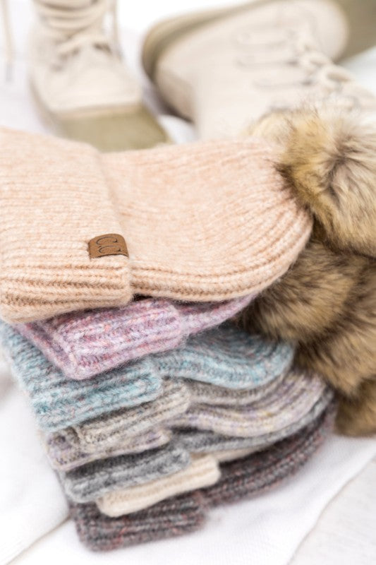 Stack of Shophouse Northwest CC marled pom beanie in neutral marled colors with faux fur pom and boots