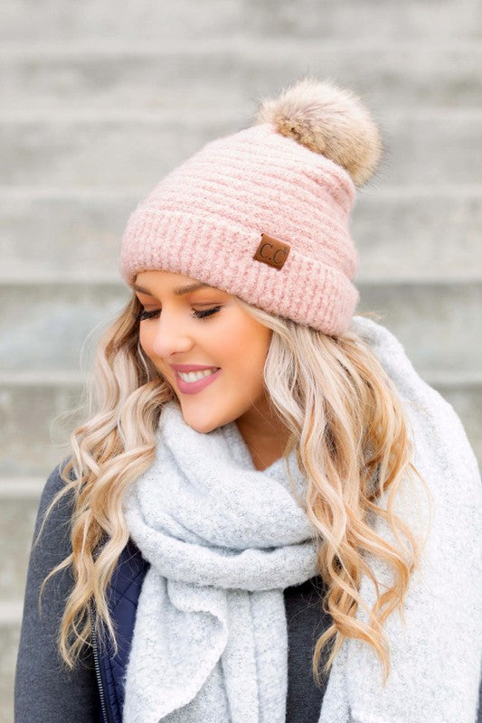 Shophouse Northwest model wearing a pink ultra soft fur pom beanie with a cozy gray scarf on stone steps