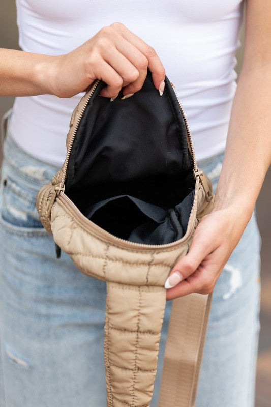 Beige Skyler puffer sling bag open to show black lined interior held by woman in white tank and jeans