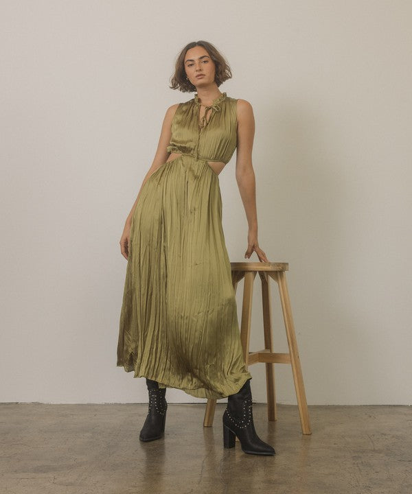 Shophouse Northwest model in olive pleated cutout dress leaning on stool wearing studded mid calf ankle boots