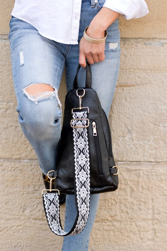 Shophouse Northwest black leather sling bag with patterned strap held by woman in ripped jeans everyday sling bag for women