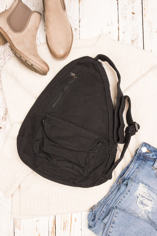 Black oversized canvas sling bag with front zip pocket and adjustable strap styled with sweater and jeans