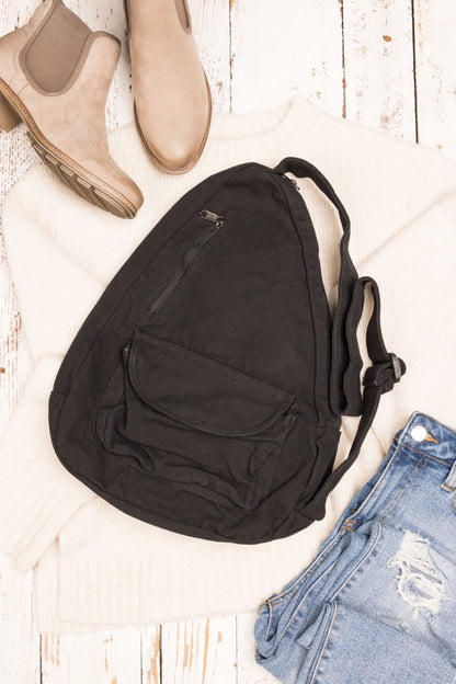 Black oversized canvas sling bag with front zip pocket and adjustable strap styled with sweater and jeans