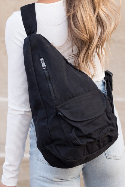 Shophouse Northwest oversized canvas sling bag in black worn crossbody on woman with long hair and zipper pockets