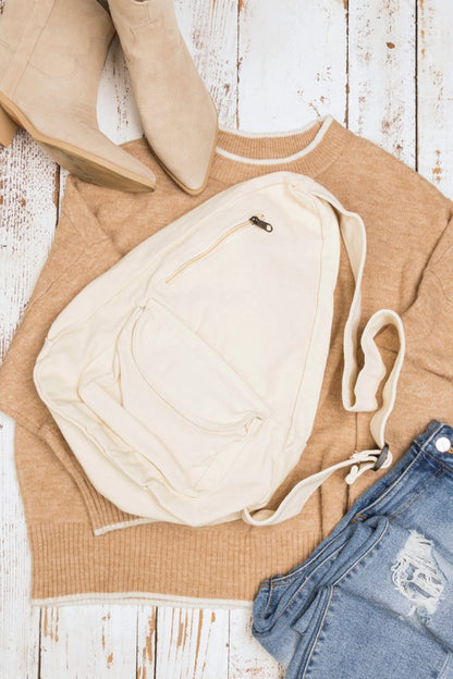Shophouse Northwest oversized canvas sling bag in cream laid on sweater with jeans and boots