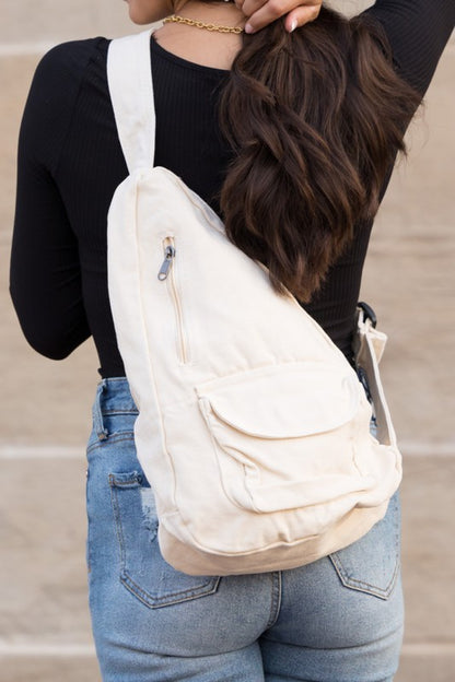 Shophouse Northwest oversized canvas sling bag in cream worn crossbody by woman with black top and jeans