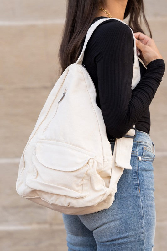 Shophouse Northwest oversized canvas sling bag in cream worn crossbody with front pocket and adjustable strap