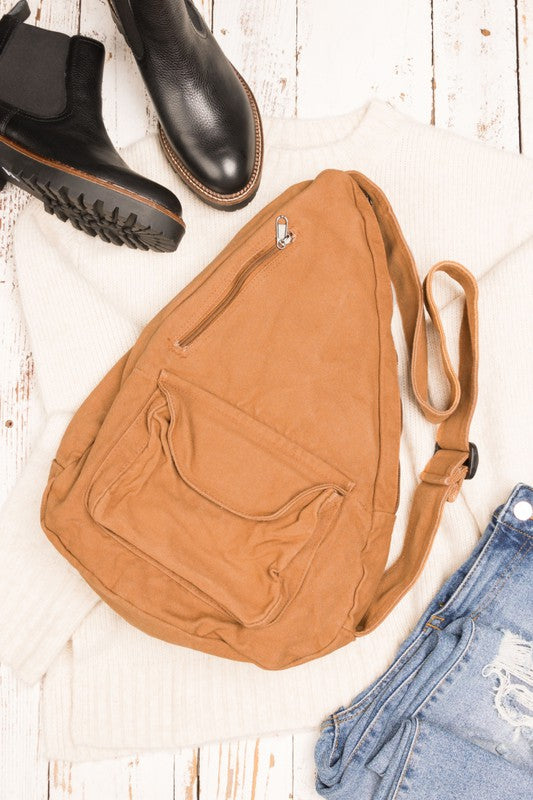 Shophouse Northwest oversized canvas sling bag in tan with front pocket and adjustable strap styled with boots and jeans