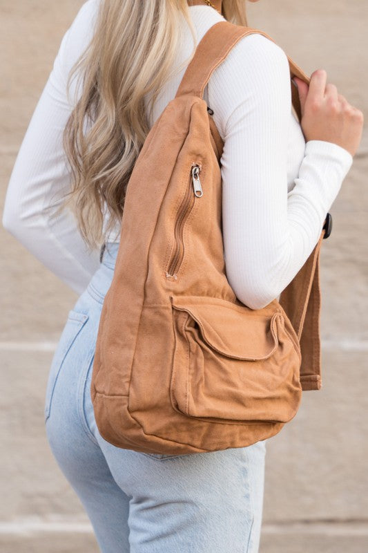Shophouse Northwest oversized canvas sling bag in tan with zip and flap pockets worn crossbody by model