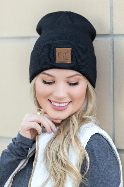 Smiling woman wearing black CC heathered boyfriend beanie with tan leather CC patch and casual layered vest