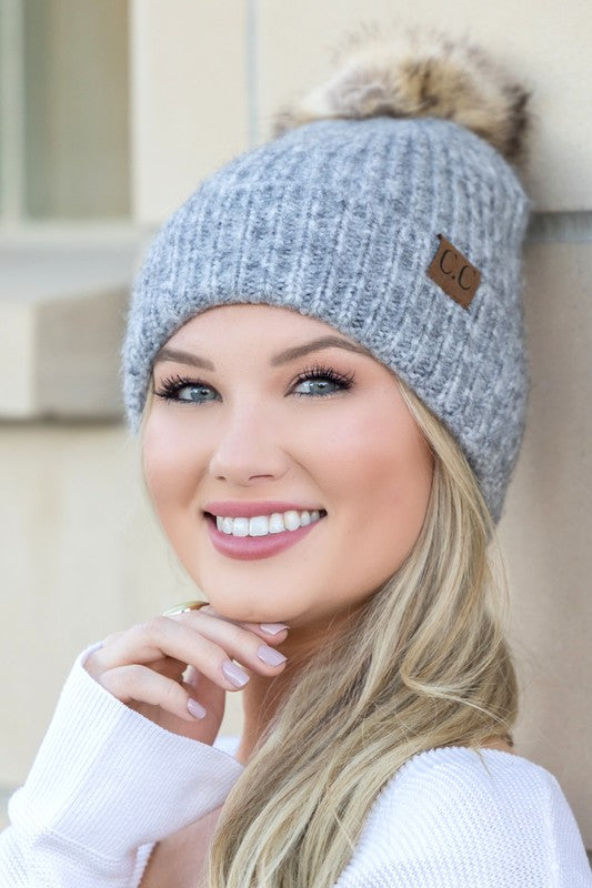 Smiling woman wearing CC marled pom beanie gray ribbed knit with faux fur pom and leather CC patch