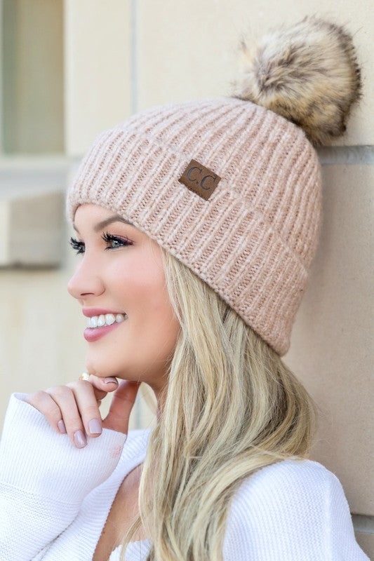 Smiling woman wearing CC marled pom beanie in blush ribbed knit with faux fur pom and leather CC patch
