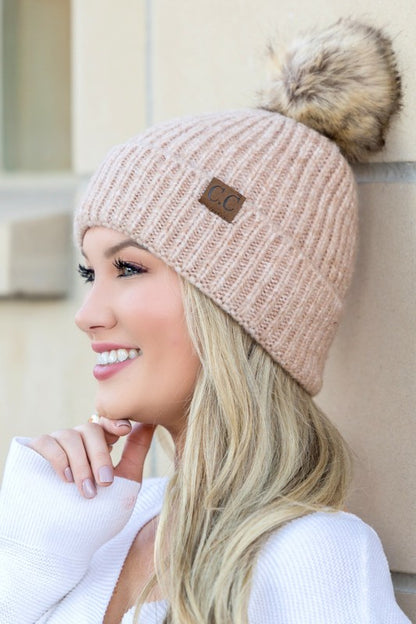 Smiling woman wearing CC marled pom beanie in blush ribbed knit with faux fur pom and leather CC patch