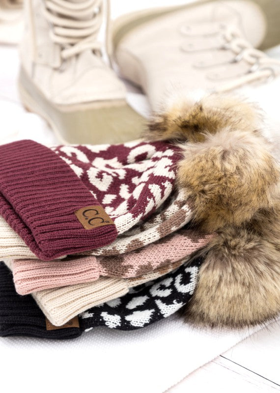 Shophouse Northwest leopard fur knit pom beanie stack in mixed colors with faux fur pom and winter boots