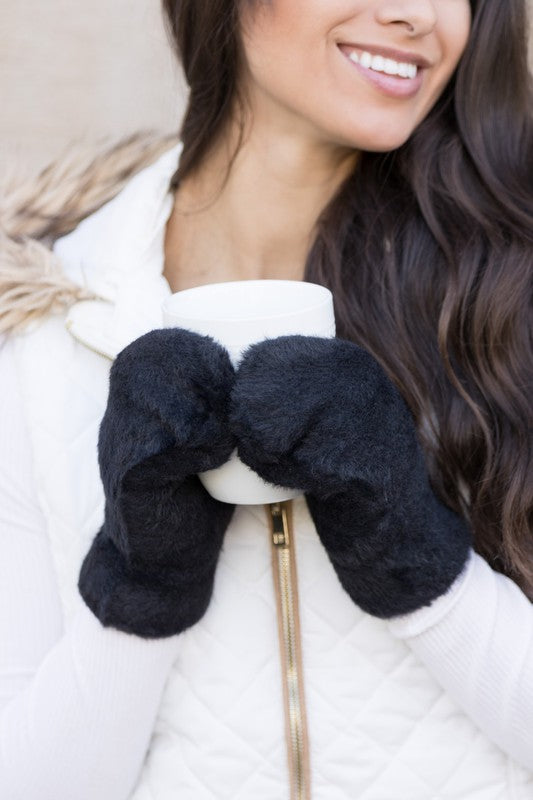 Shophouse Northwest black plush fur lined mittens on woman holding white mug wearing white quilted coat