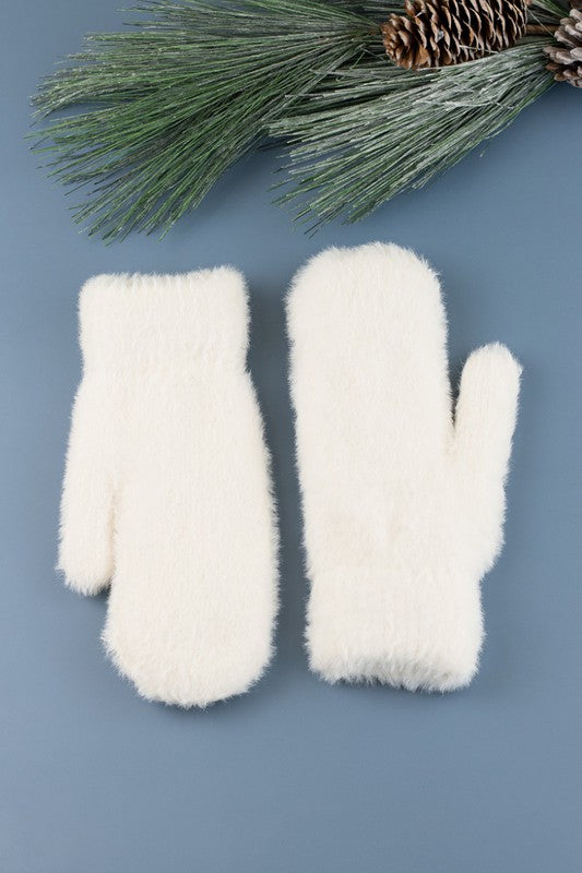Shophouse Northwest cream plush fur lined mittens pair on blue background with pine branch holiday styling