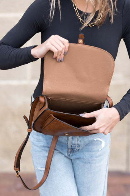 Shophouse Northwest foldover buckle crossbody bag open to show lined interior pockets in brown leather worn over shoulder