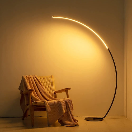 Modern curve floor lamp illuminating a cozy chair with a soft blanket, enhancing the room's ambiance