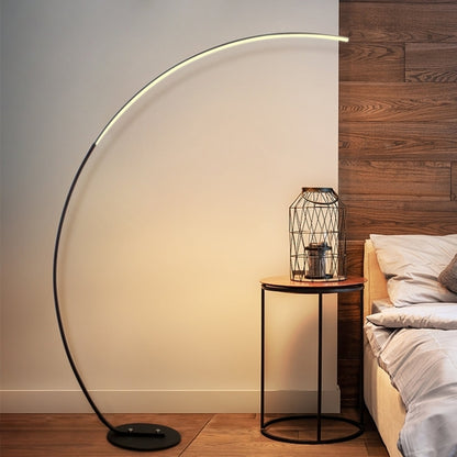 Elegant modern curve floor lamp in black, adding stylish illumination to a cozy bedroom setting