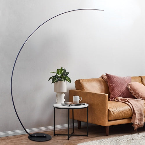Elegant modern curve floor lamp with a sleek design beside a cozy sofa in a stylish living room