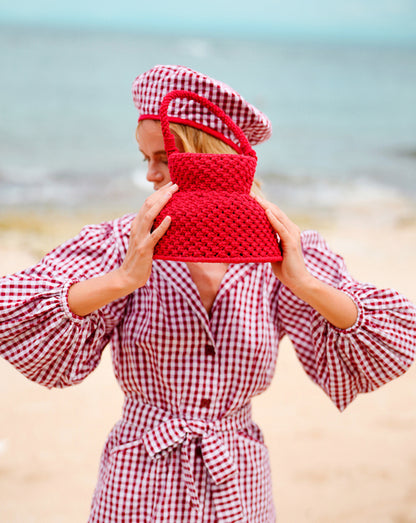 Stylish woman on the beach holding a red macrame basket bag with matching accessories