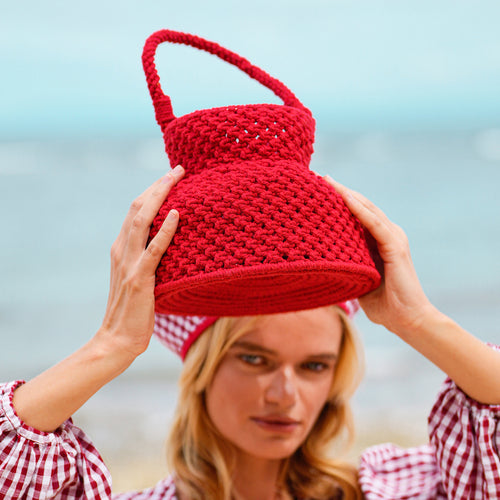 Woman holding a red macrame basket bag against a beach backdrop for summer outings