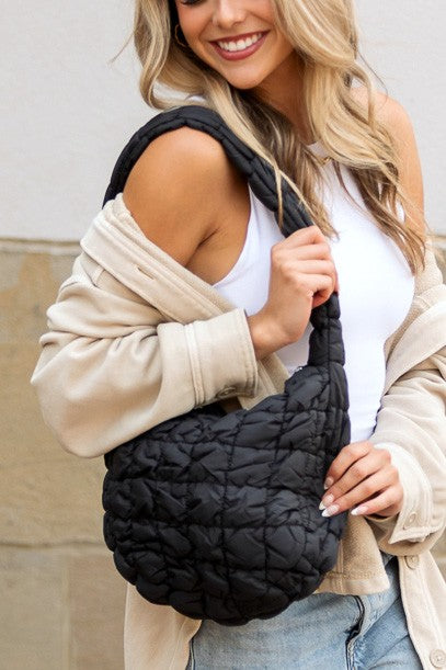 Shophouse Northwest black quilted puffer shoulder bag worn by woman with white tank and beige jacket