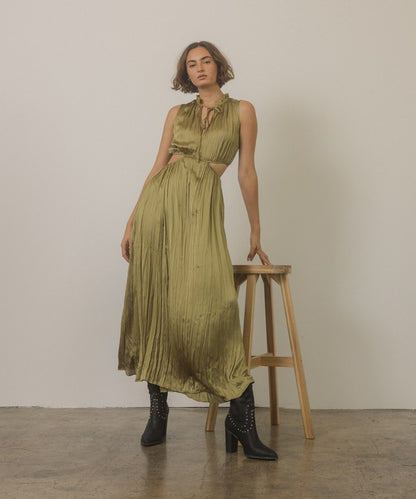 Shophouse Northwest model in olive pleated cutout dress leaning on stool wearing studded mid calf ankle boots