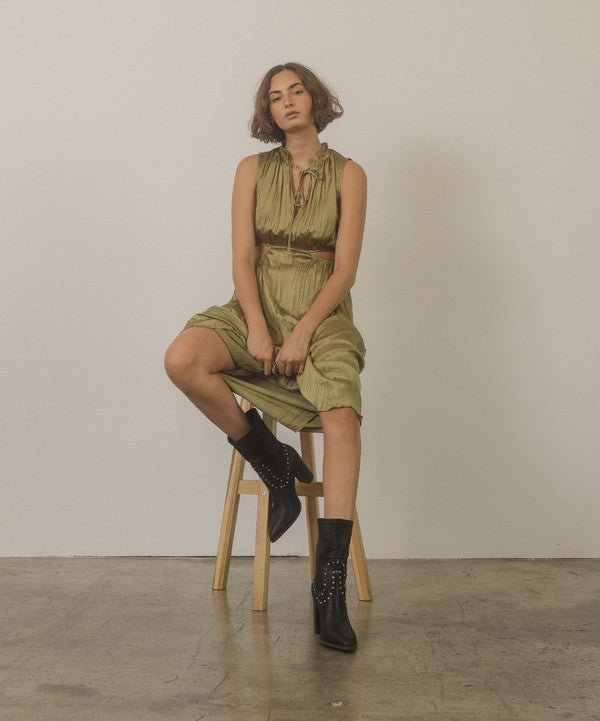 Shophouse Northwest model wearing olive green dress seated on stool showcasing studded mid calf ankle boots in black