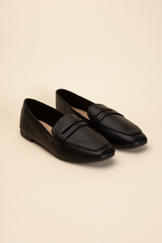 Harriet-8 slip on penny flats shoes by Shophouse Northwest black leather penny loafers on beige background