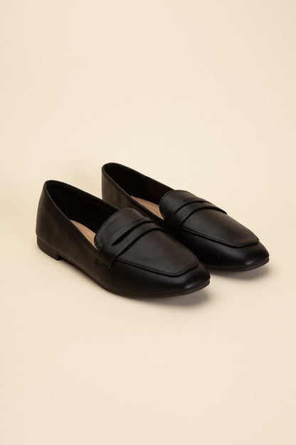 Harriet-8 slip on penny flats shoes by Shophouse Northwest black leather penny loafers on beige background