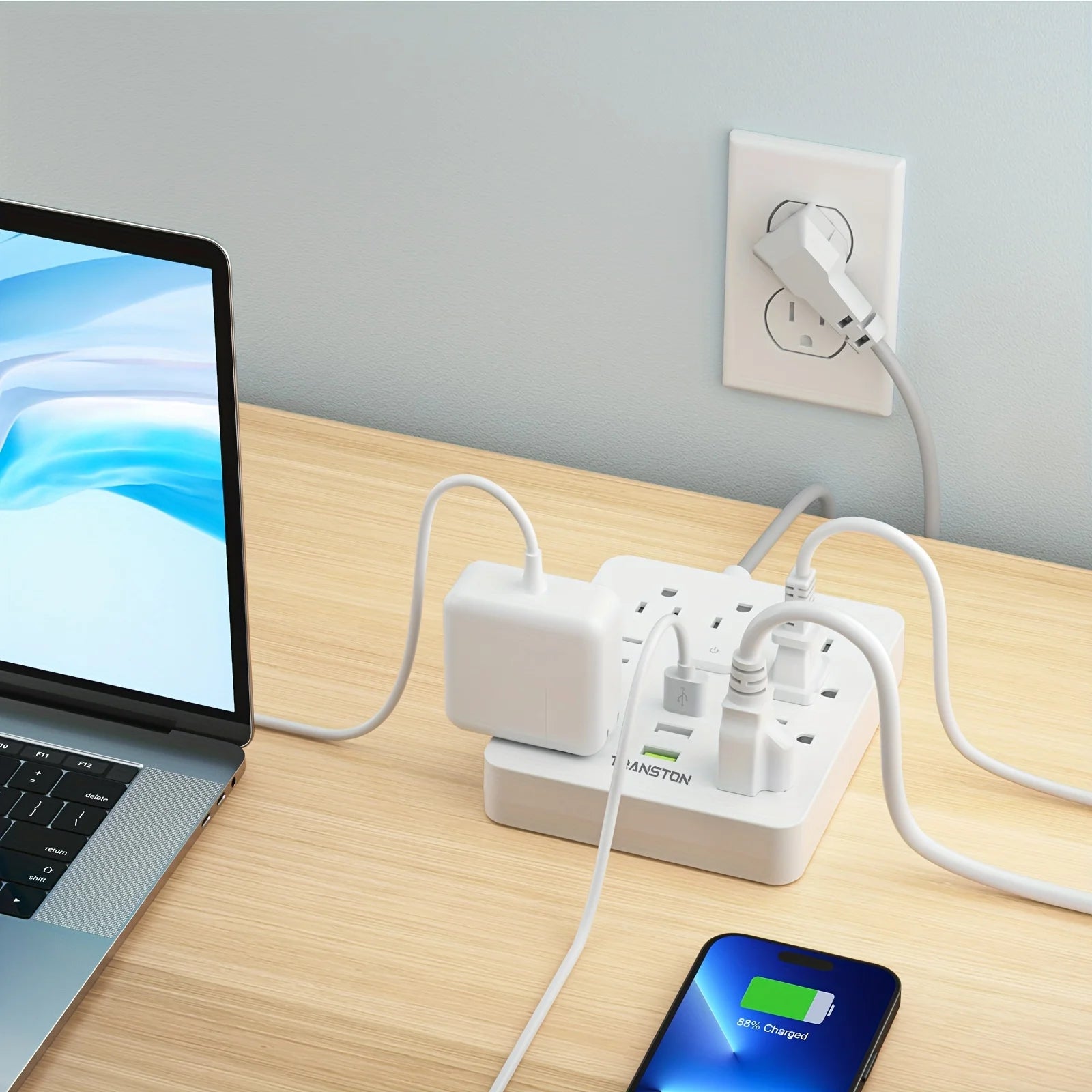 White surge protector power strip with usb connected to multiple devices including a laptop and smartphone on wooden desk