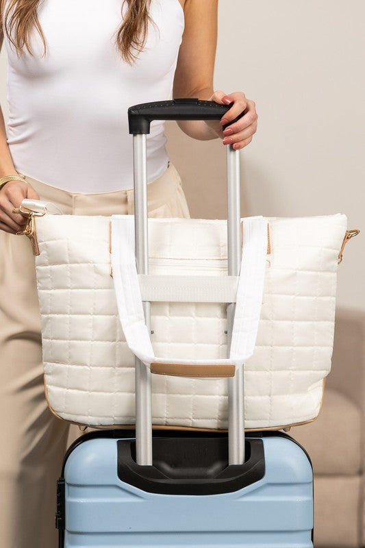 Shophouse Northwest quilted travel tote bag cream with luggage sleeve on blue suitcase and woman holding handle