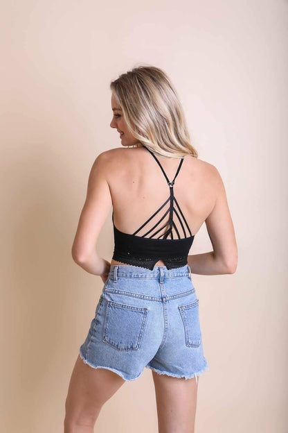 Back view of a woman wearing a trimmed halter crop top bralette with stylish straps and denim shorts
