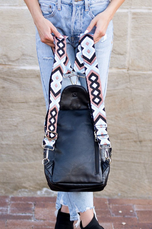 Alba backpack sling convertible bag black leather sling with patterned adjustable straps held by person in ripped jeans