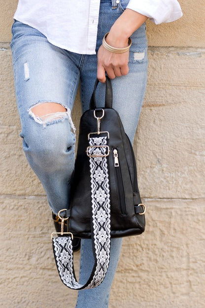 Shophouse Northwest black leather sling bag with patterned strap held by woman in ripped jeans everyday sling bag for women