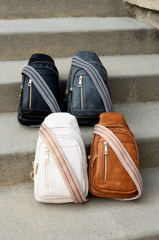 Four Genevive leather sling crossbody bag styles in black gray white and tan with woven straps on concrete steps
